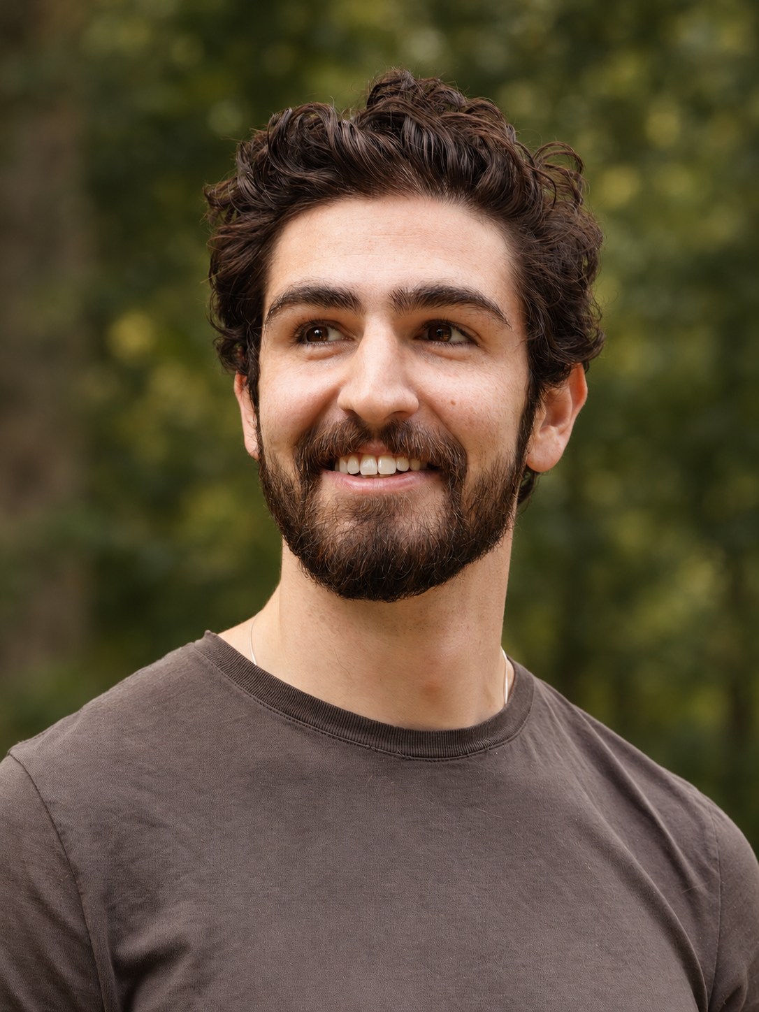Outdoor headshot with soft green foliage in the background