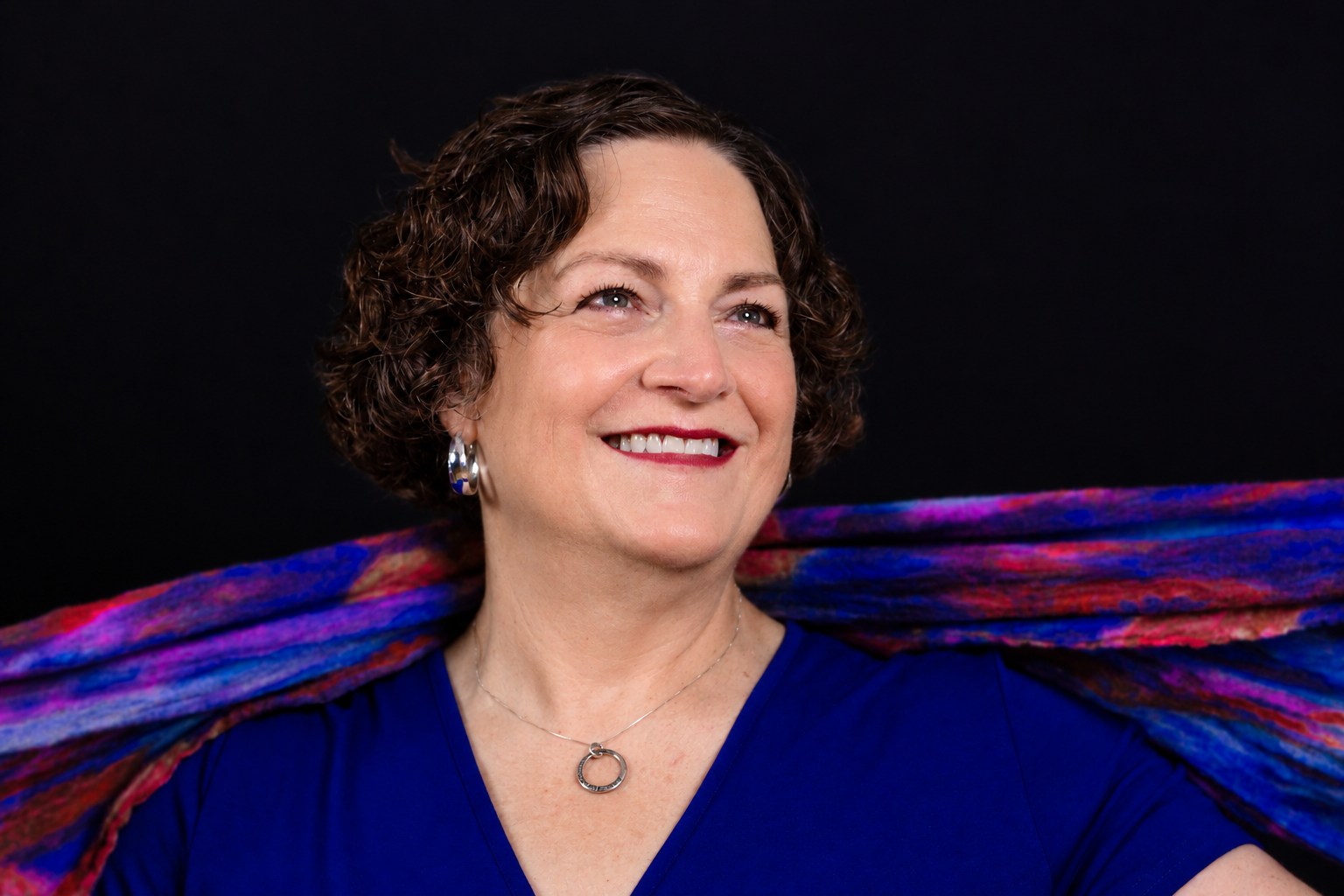 Smiling studio portrait in cobalt blue with a colorful flowing scarf