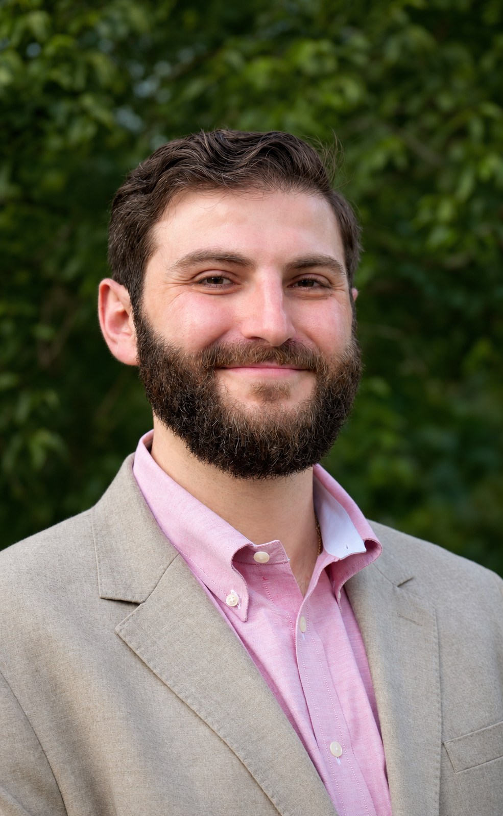 Outdoor portrait in a light jacket and pink shirt against green foliage