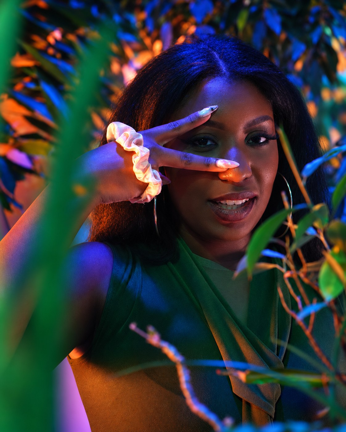 Playful peace-sign portrait framed by leaves and vivid colored light