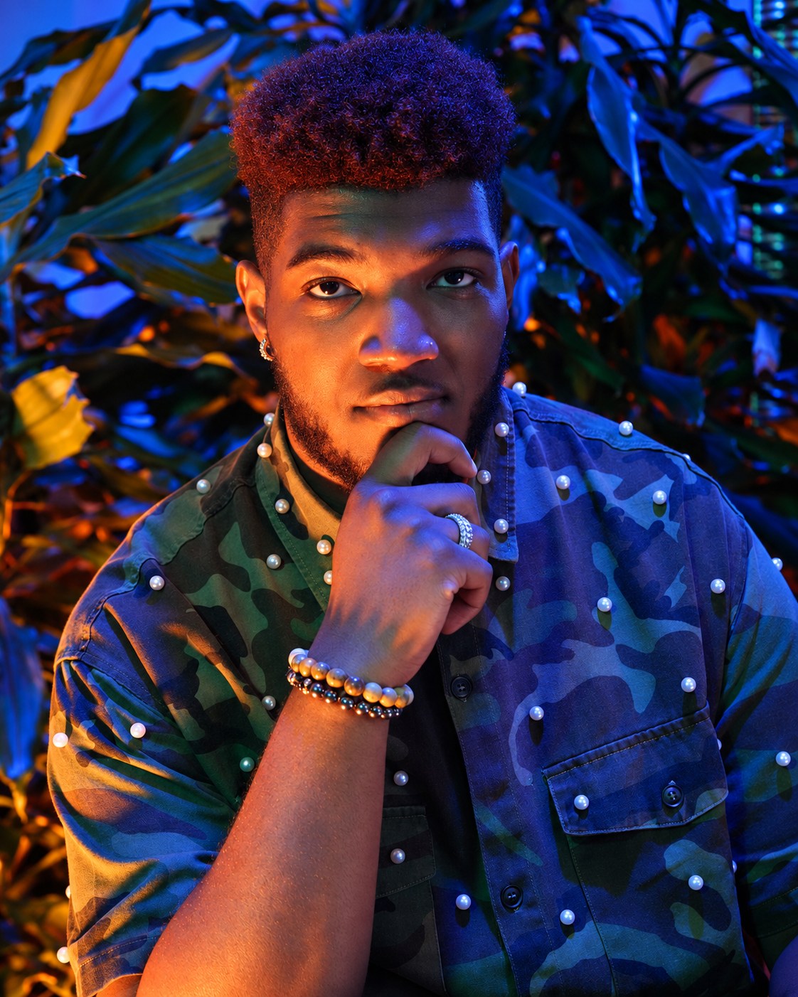 Portrait with a hand at the chin and a pearl-adorned shirt in blue and amber light