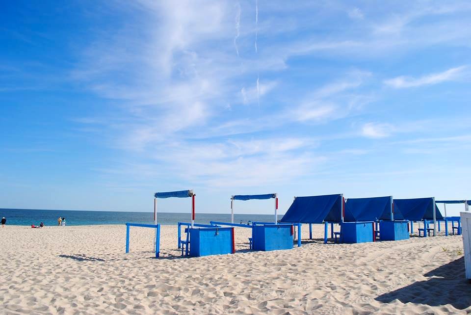 Blue beach huts beside a sandy beach and calm sea