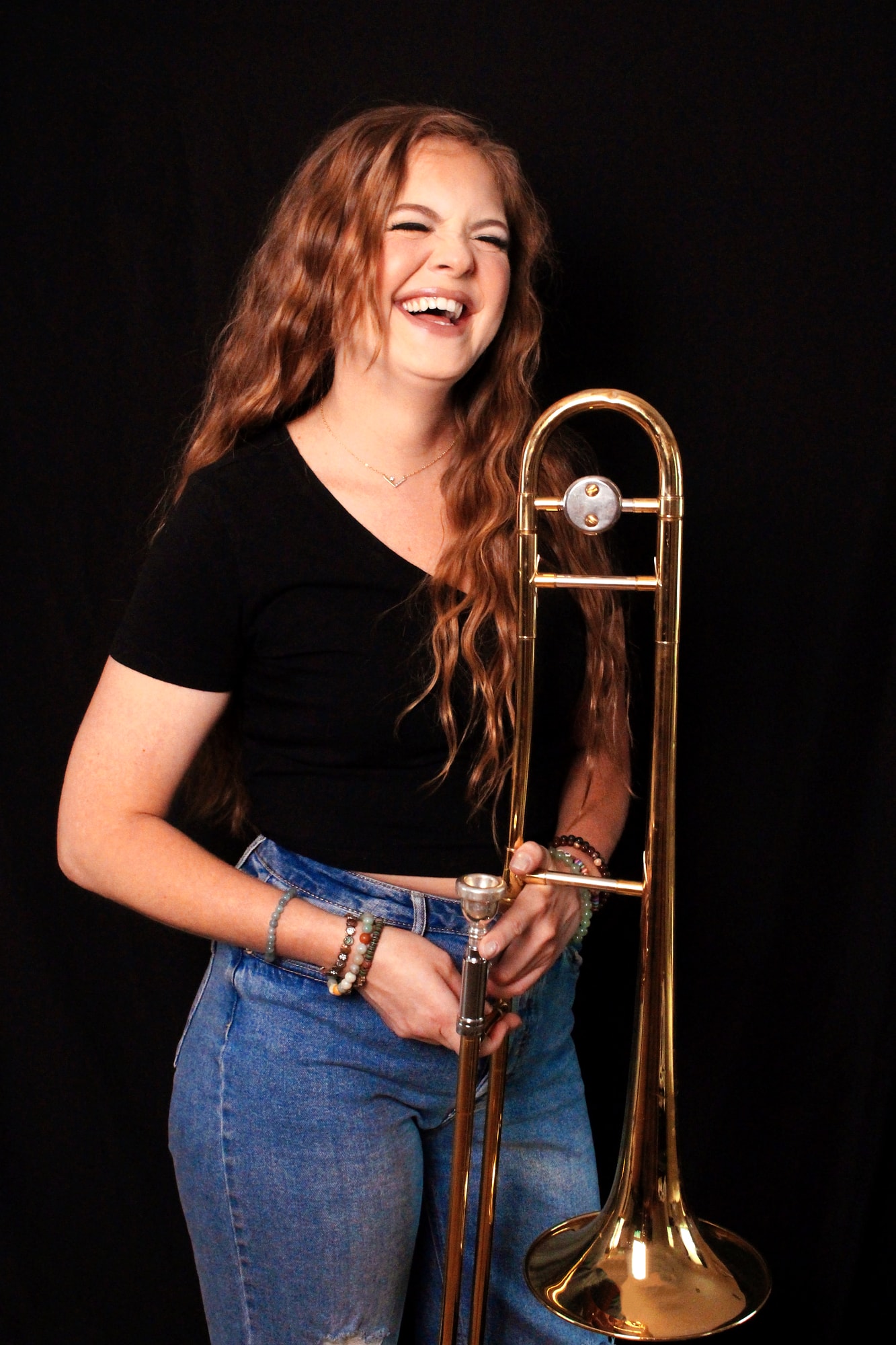 Laughing musician holding a trombone against a dark studio background