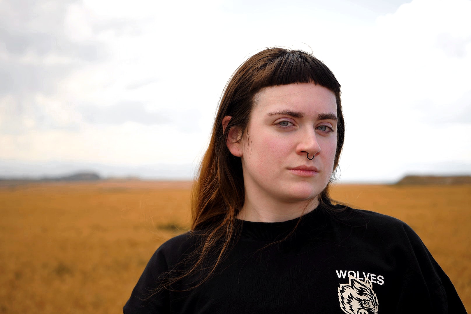 Portrait in a black shirt beneath a cloudy sky in an open field