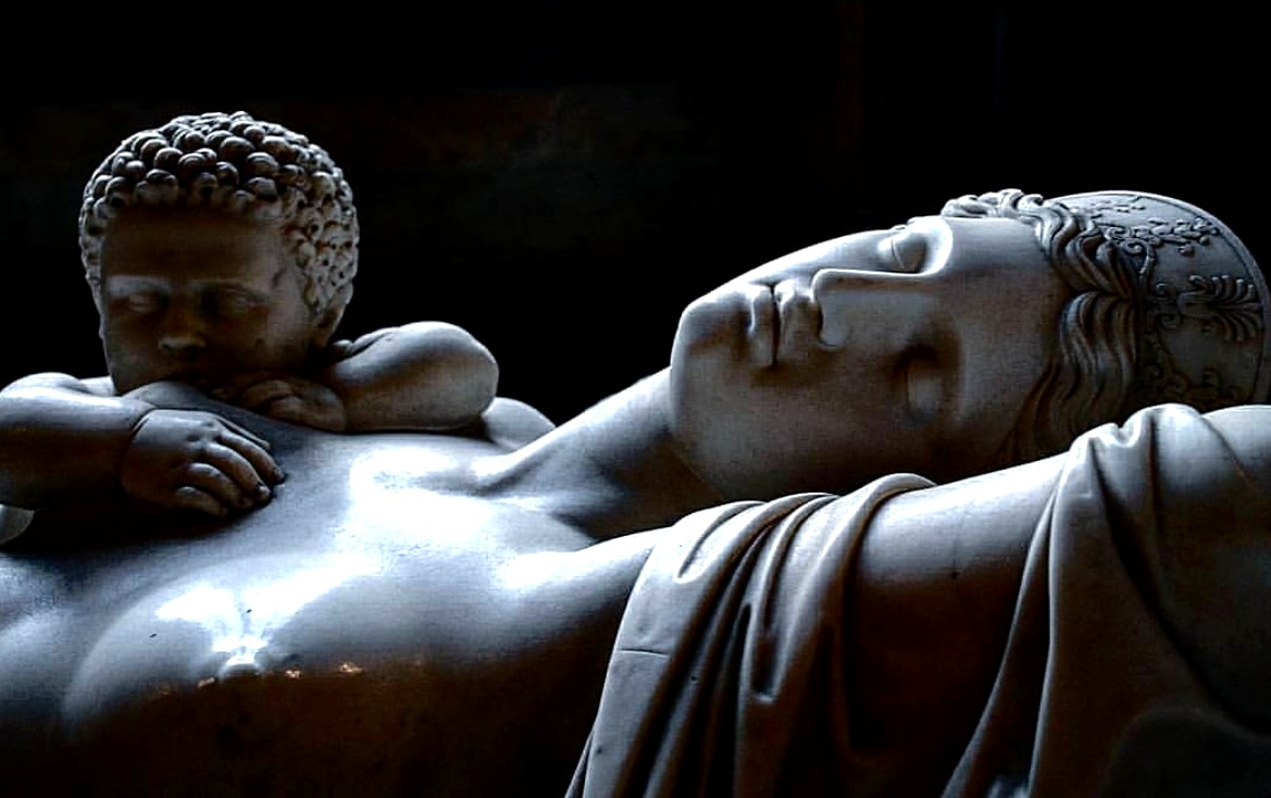 Reclining stone sculpture and cherub illuminated against a dark background