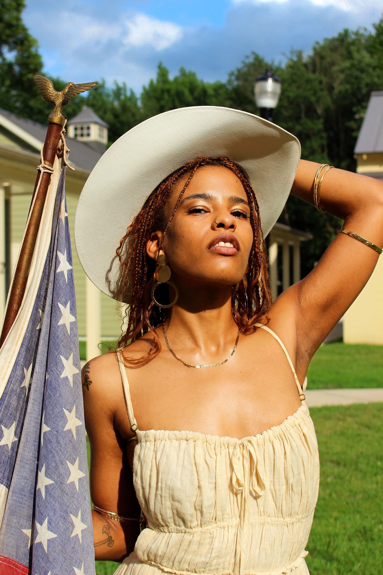 Sunlit portrait in a cream dress and cowboy hat beside an American flag