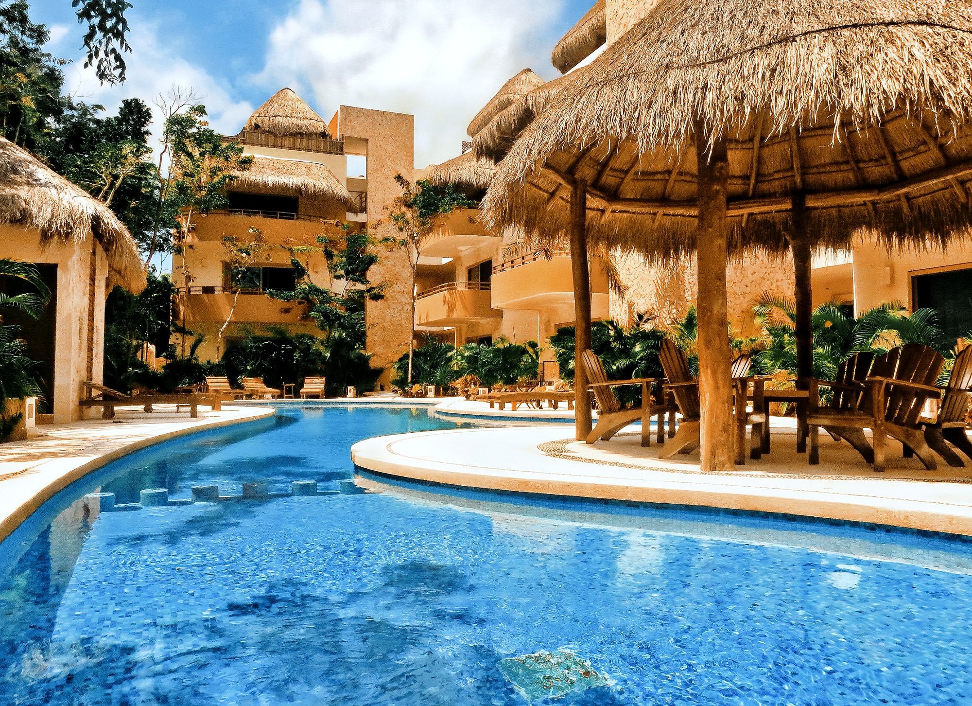 Curved blue swimming pool surrounded by palms and thatched roofs
