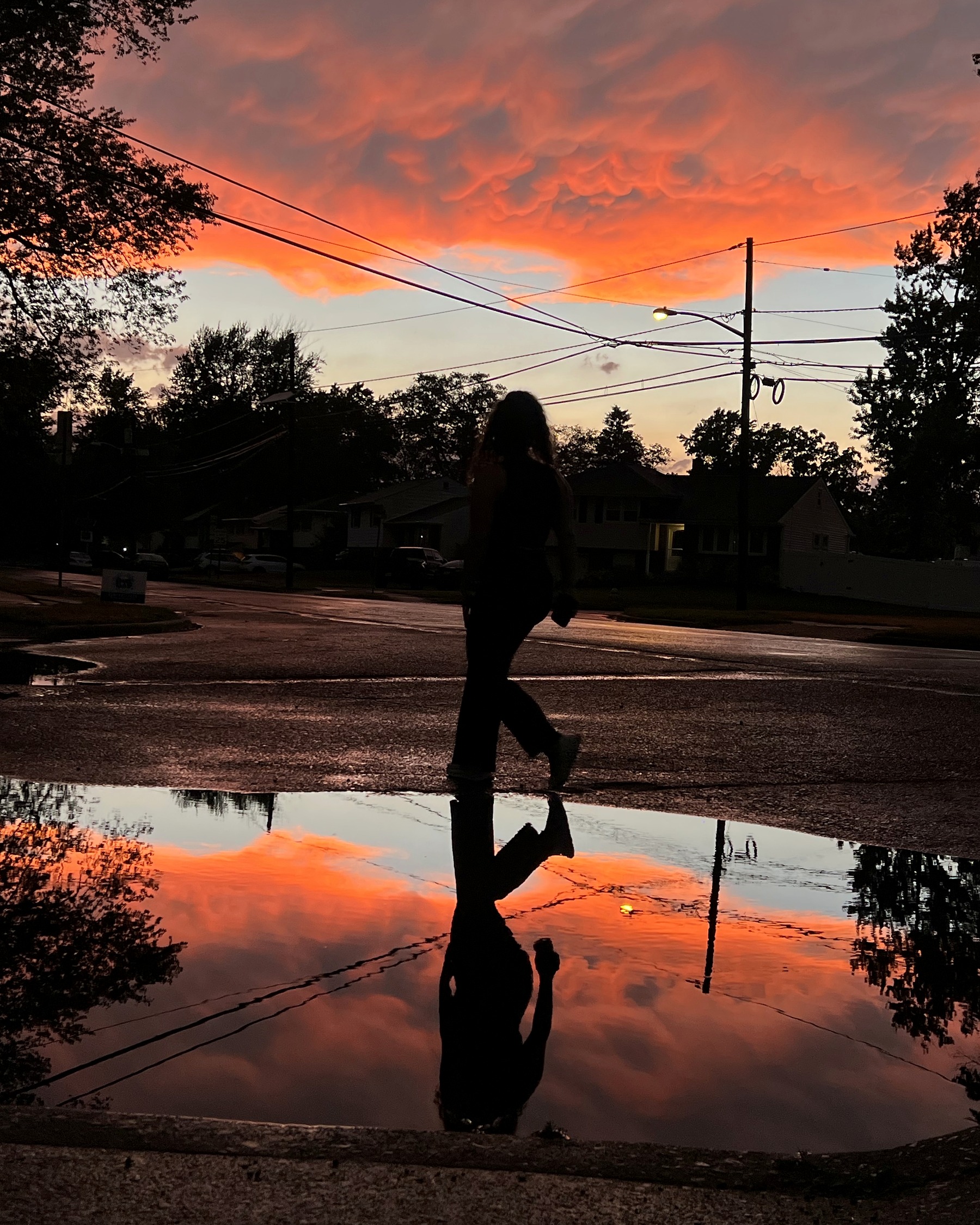 Silhouette beneath orange sunset clouds reflected in a street puddle