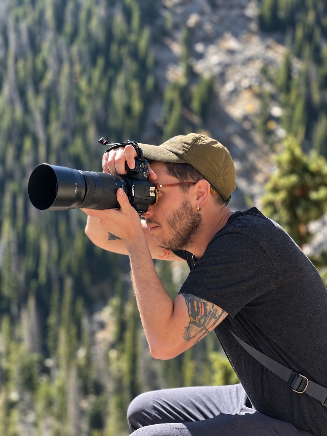Photographer holding a camera against a softly blurred mountain forest